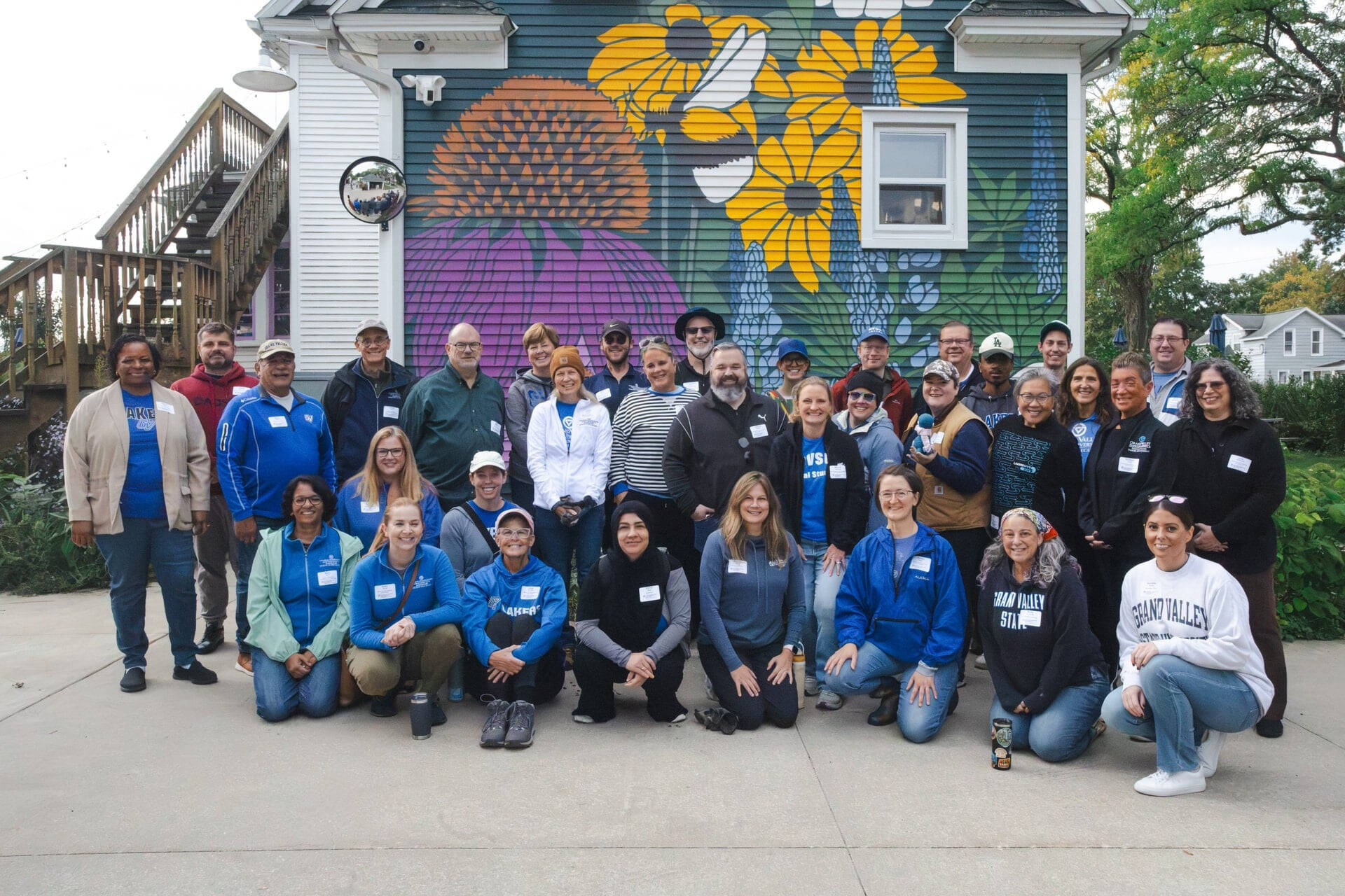 large group of people standing and sitting outside a building that has a mural of flowers painted on it